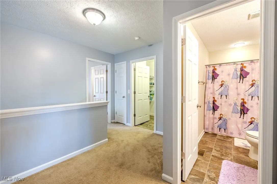 Corridor featuring light colored carpet and a textured ceiling