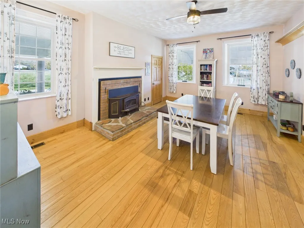 Dining space with a wood stove, light wood-style floors, a textured ceiling, and a ceiling fan