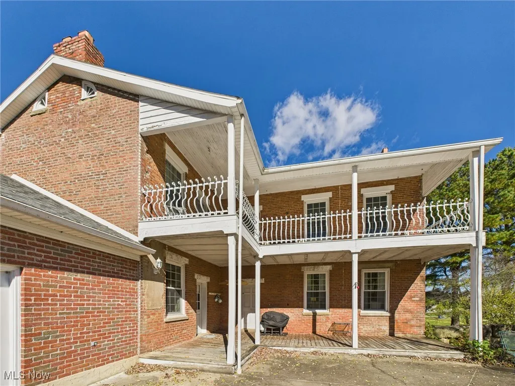 Rear view of property featuring a balcony, brick siding, and a patio
