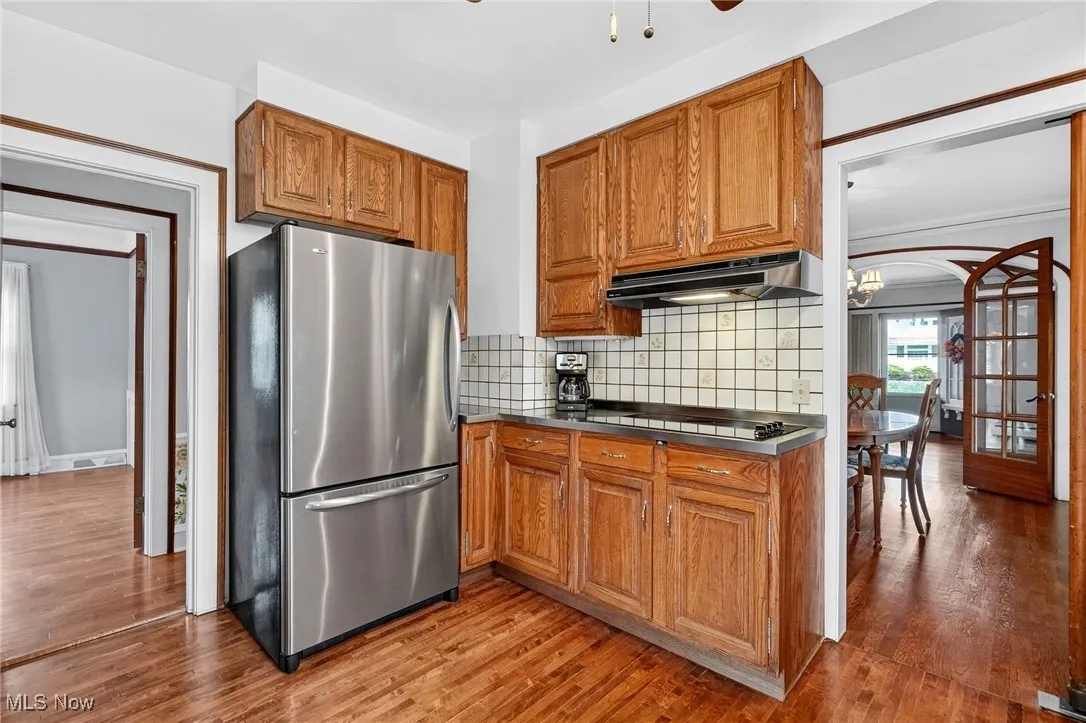 Kitchen featuring freestanding refrigerator, wood cabinets, tasteful backsplash, light wood-style flooring, and under cabinet range hood