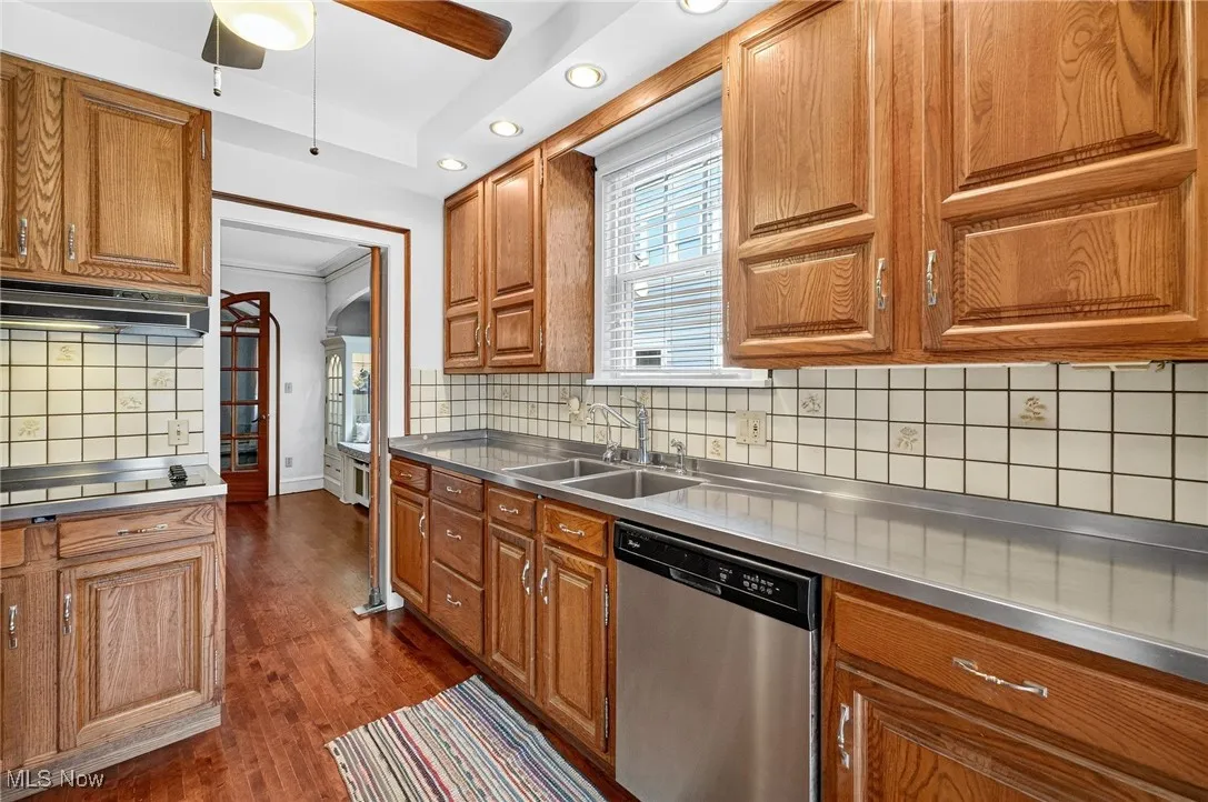 Kitchen featuring stainless steel countertops, wood cabinets, dishwasher, tasteful backsplash, and dark wood-style flooring