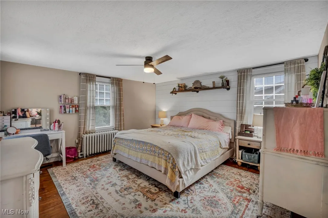 Bedroom with wood finished floors, radiator heating unit, a textured ceiling, multiple windows, and a ceiling fan