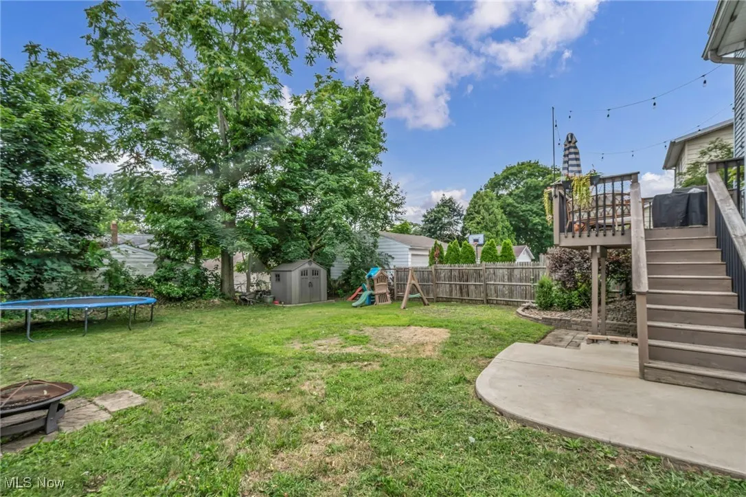 Fenced backyard with a playground, a trampoline, a fire pit, a patio, and a storage shed