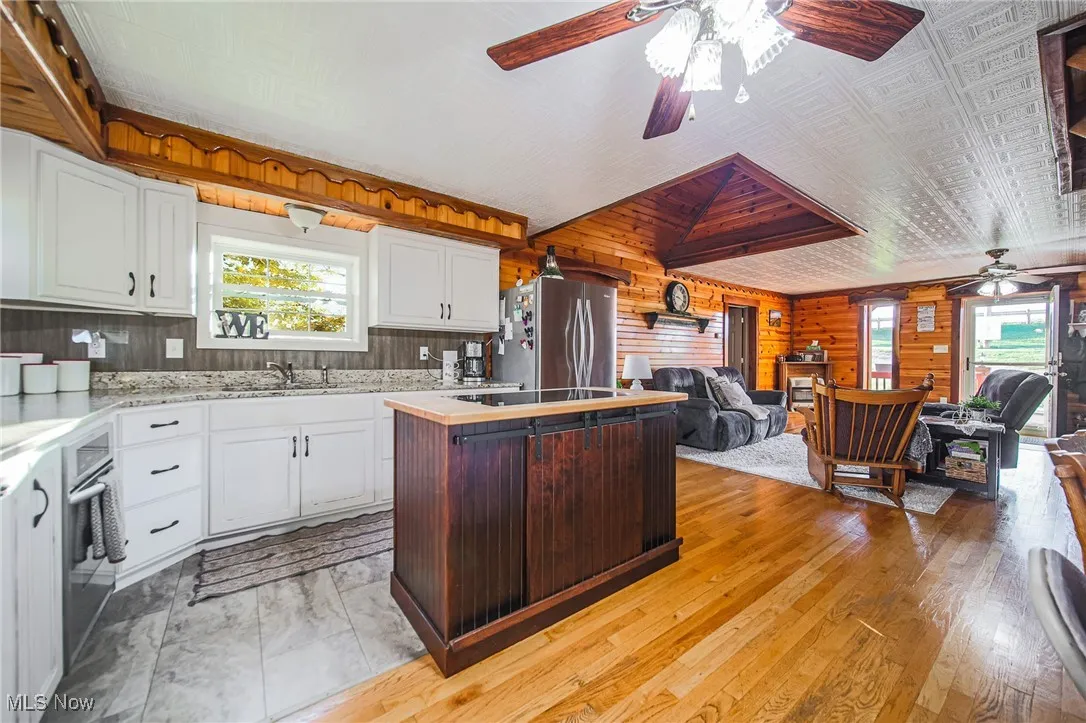 Kitchen with white cabinets, wooden walls, ceiling fan, a center island, and appliances with stainless steel finishes