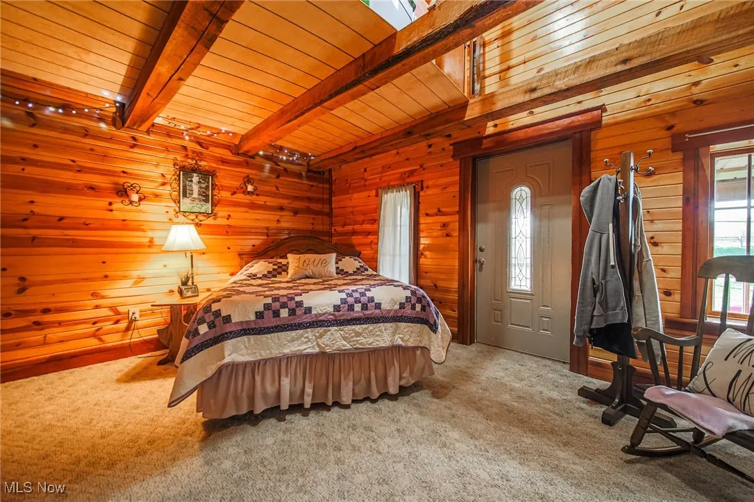 Bedroom featuring wooden walls, carpet flooring, and a wooden ceiling with exposed beams