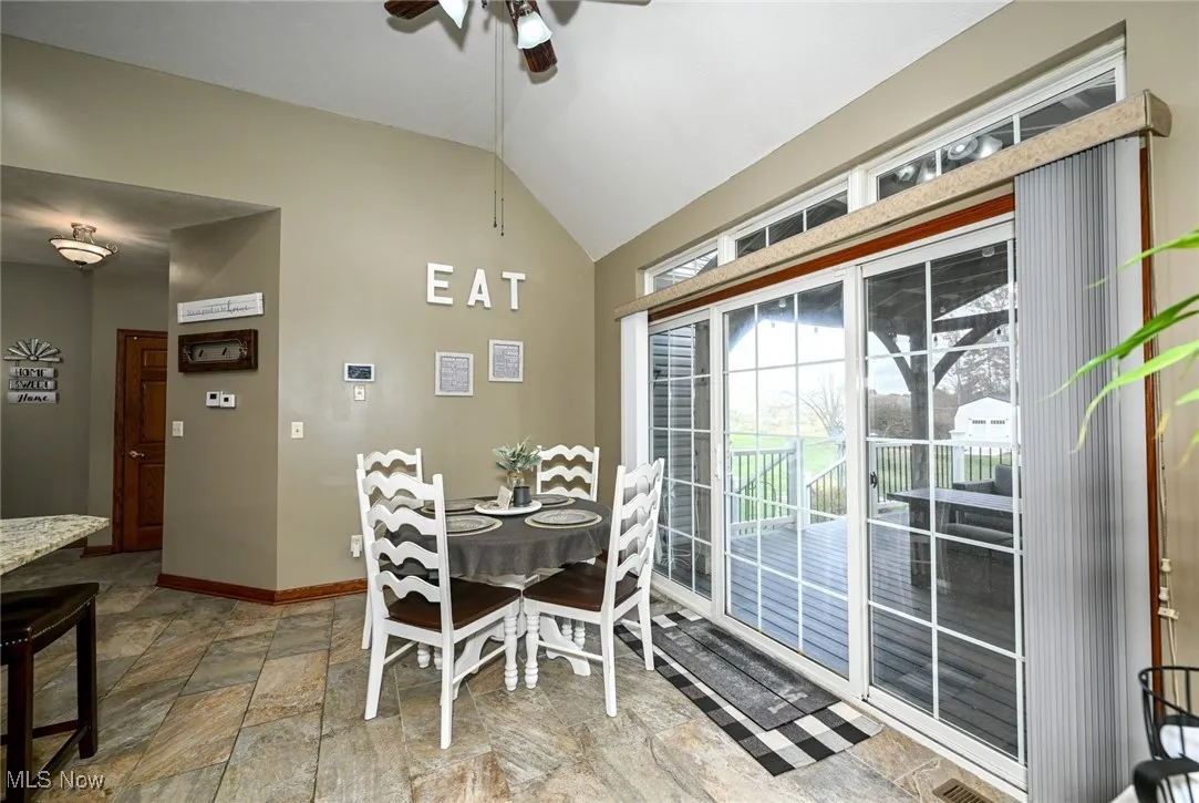 Dining area with lofted ceiling, a ceiling fan, and light ceramic stone finish flooring. Sliders leading to covered deck