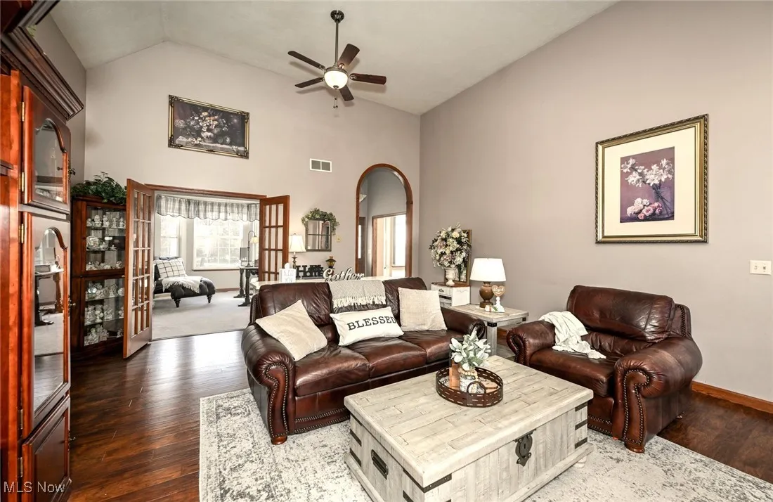 Living area with arched walkways, french doors, a ceiling fan, dark wood-style floors, and high vaulted ceiling