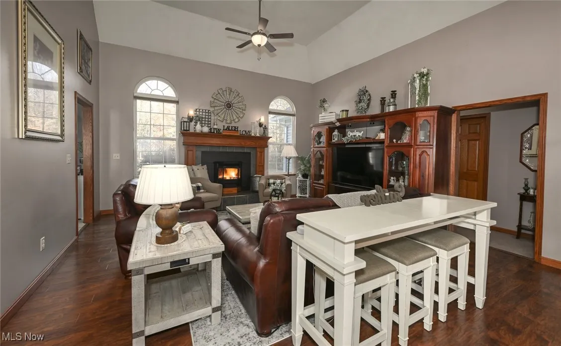 Living area with a lit fireplace, dark laminate wood finished floors, ceiling fan, and lofted ceiling