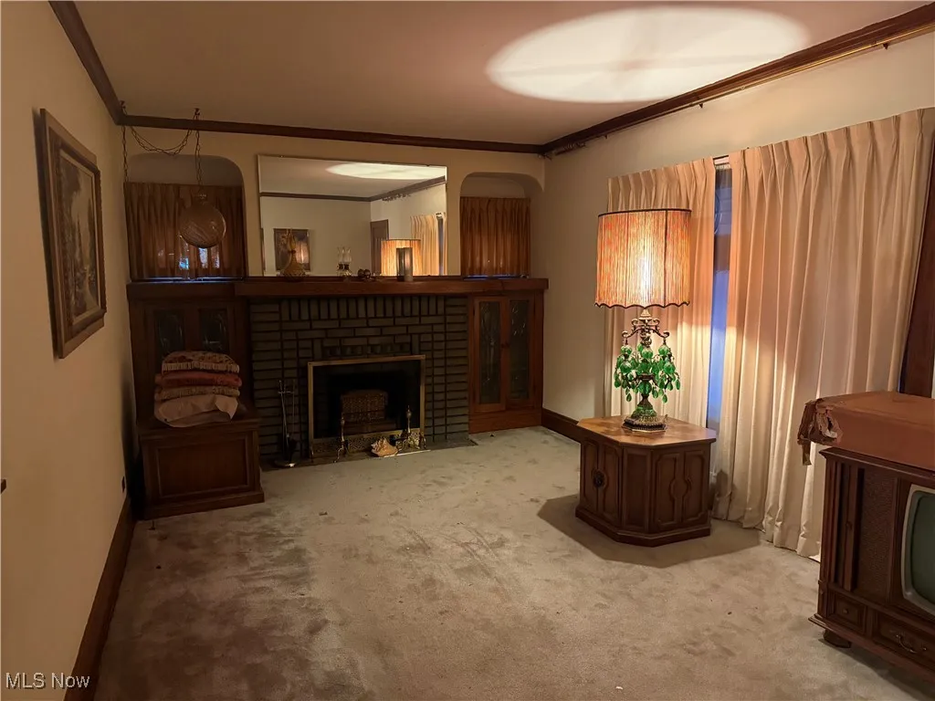 Living area featuring a brick fireplace, ornamental molding, and carpet flooring