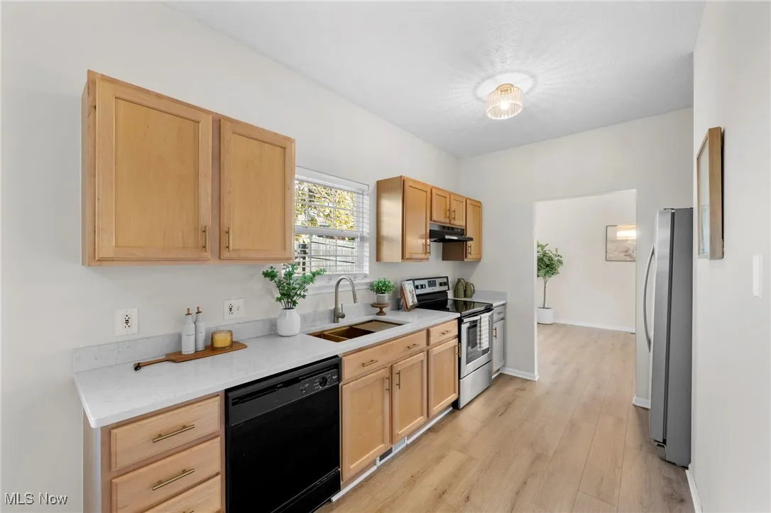 Kitchen with stainless steel appliances, light wood-type flooring, light brown cabinets, light stone countertops, and under cabinet range hood
