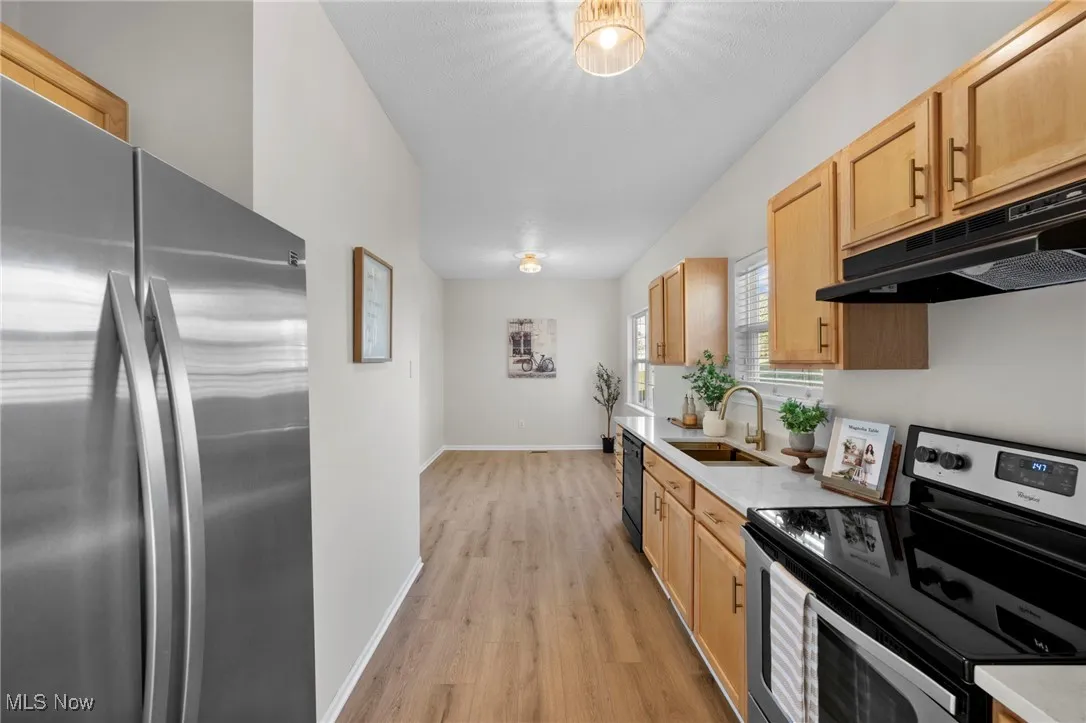 Kitchen with appliances with stainless steel finishes, light wood-type flooring, under cabinet range hood, light brown cabinetry, and light stone counters