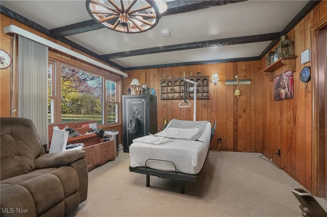 Bedroom featuring beam ceiling, wooden walls, light colored carpet, and a chandelier