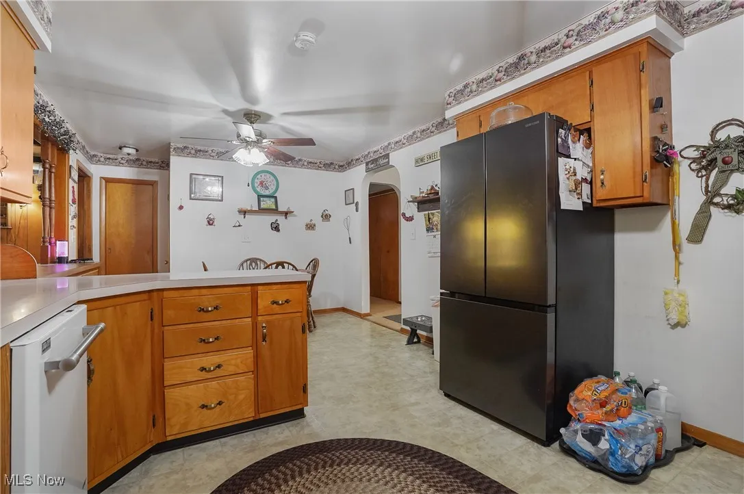 Kitchen with arched walkways, brown cabinetry, freestanding refrigerator, light countertops, and dishwasher