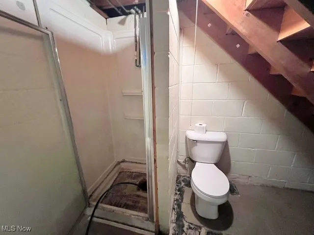 Full bath featuring concrete block wall and a shower stall