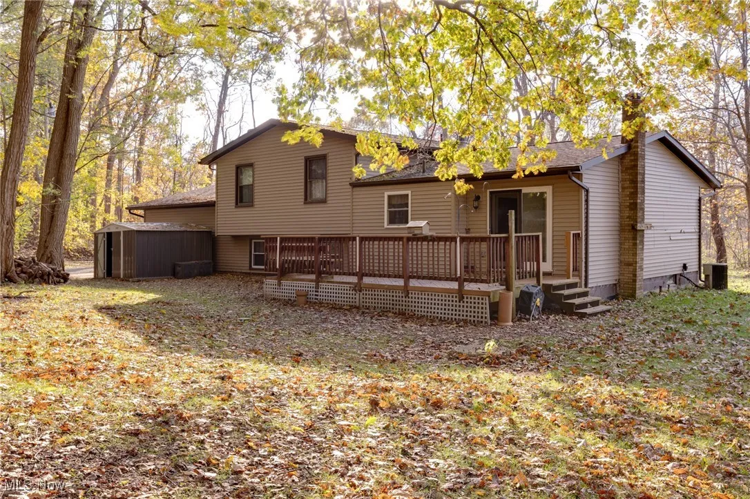Rear view of property featuring a deck, an outdoor structure, and roof with shingles