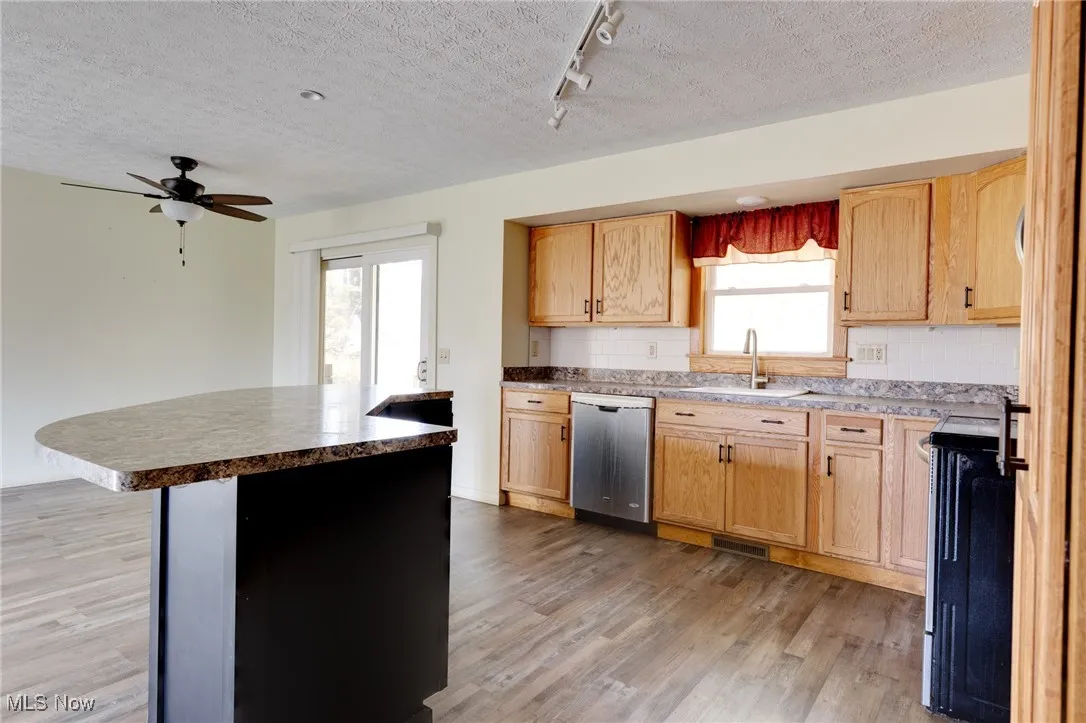 Kitchen with track lighting, range, a textured ceiling, decorative backsplash, and light wood-style flooring