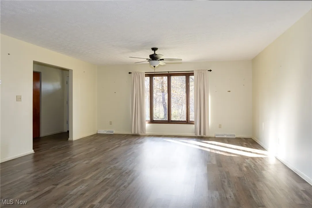 Living room with a ceiling fan, dark wood-type flooring, and a textured ceiling