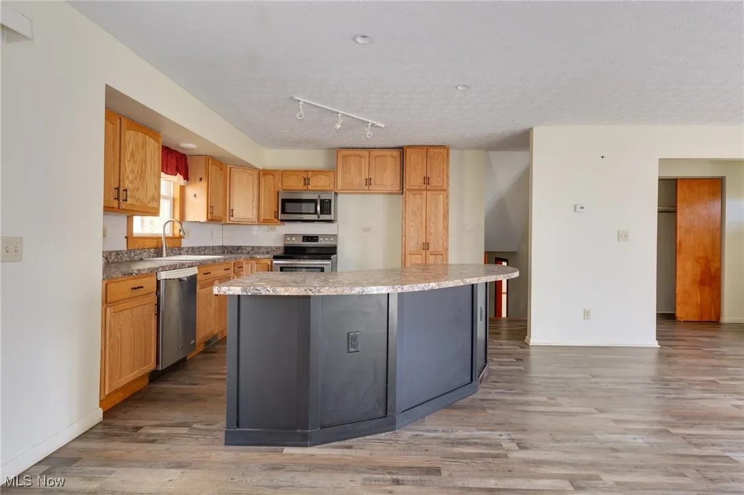 Kitchen with stainless steel appliances, light wood finished floors, light countertops, rail lighting, and a kitchen island
