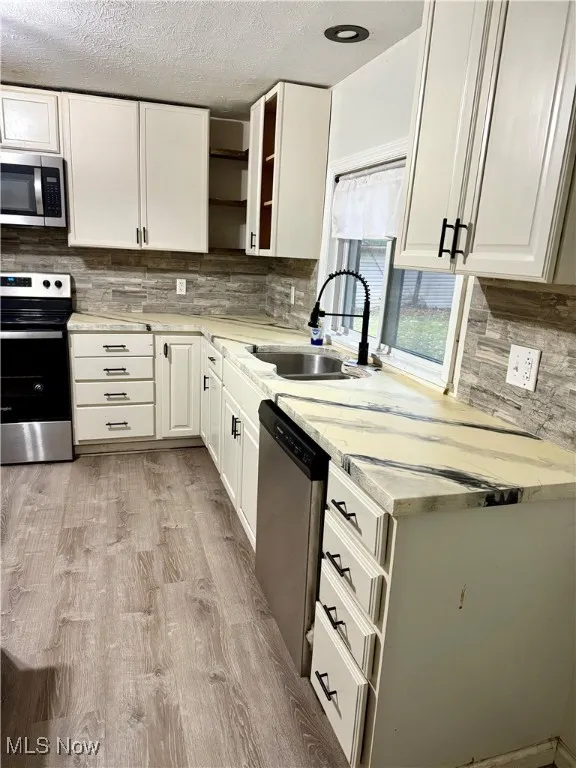 Kitchen with appliances with stainless steel finishes, open shelves, tasteful backsplash, a textured ceiling, and light wood-style flooring