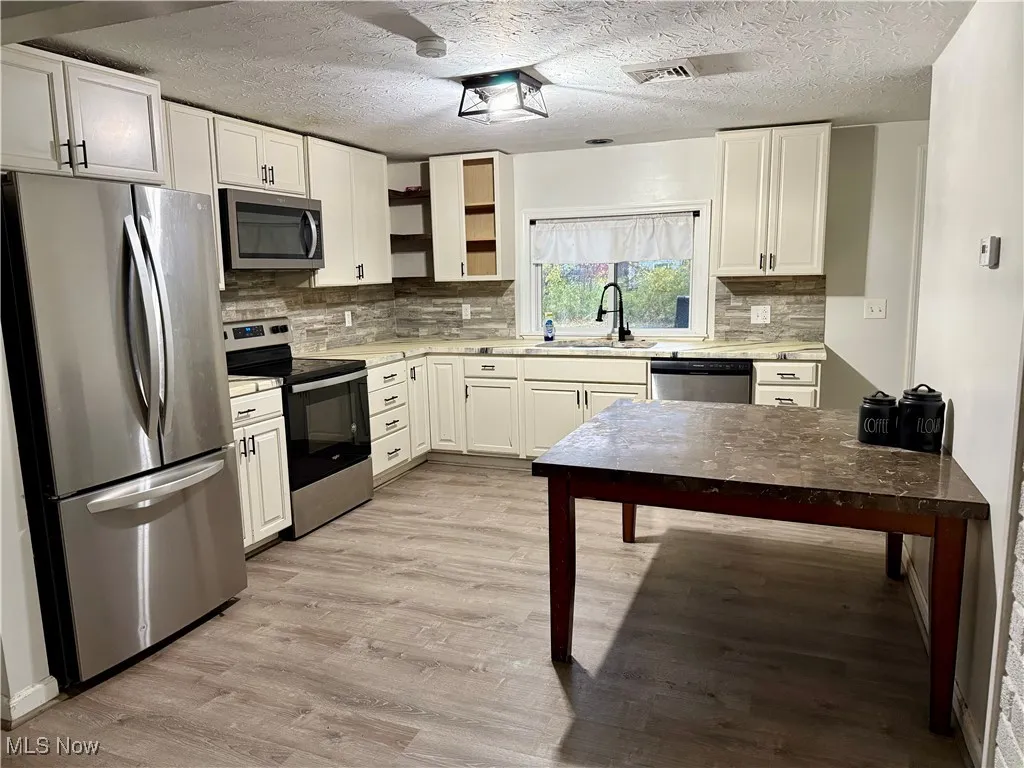 Kitchen with appliances with stainless steel finishes, light countertops, light wood-style floors, open shelves, and white cabinets