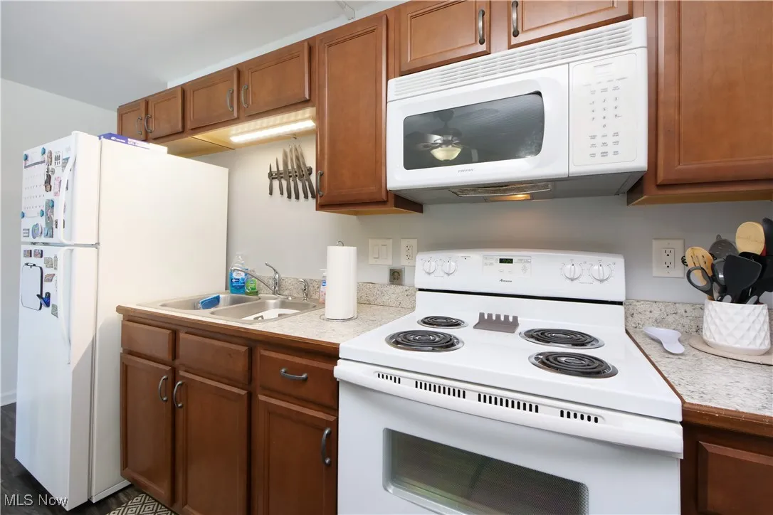Kitchen featuring white appliances, light countertops, brown cabinets, and dark wood-type flooring