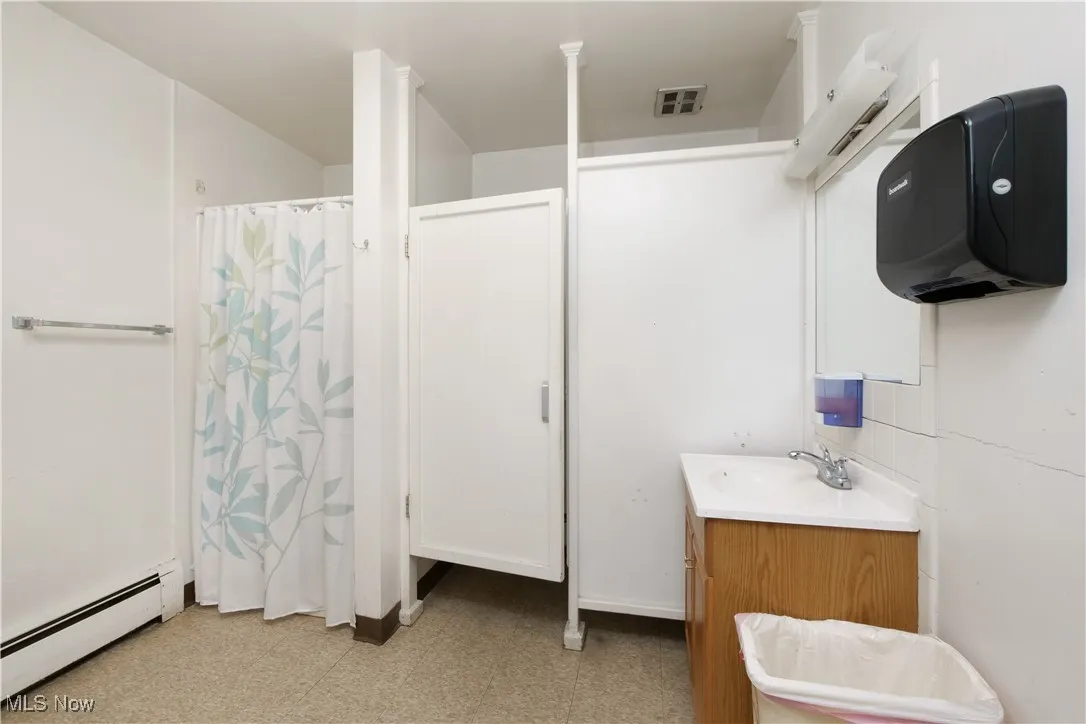 Bathroom with a baseboard heating unit, a shower with shower curtain, light floors, and vanity
