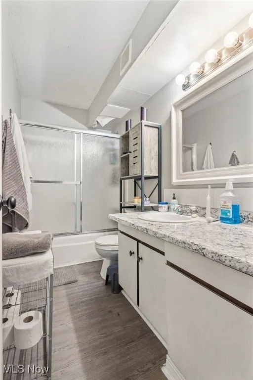 Full bathroom with vanity, dark wood-style flooring, and enclosed tub / shower combo