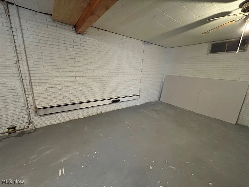 Unfinished below grade area featuring brick wall, baseboard heating, and a ceiling fan