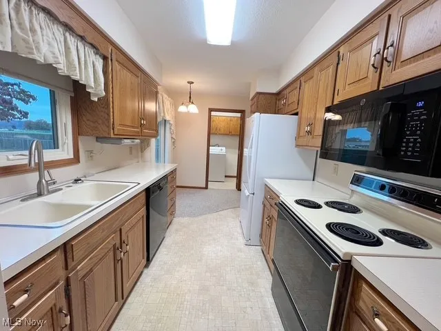 Kitchen with black appliances, brown cabinetry, light countertops, decorative light fixtures, and washer / dryer