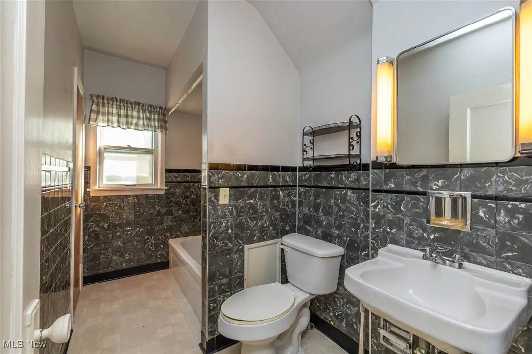 Bathroom with tile walls, a bath, and wainscoting