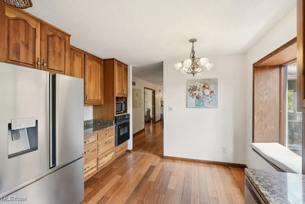 Kitchen with stainless steel appliances, dark stone countertops, pendant lighting, light wood-style flooring, and a chandelier