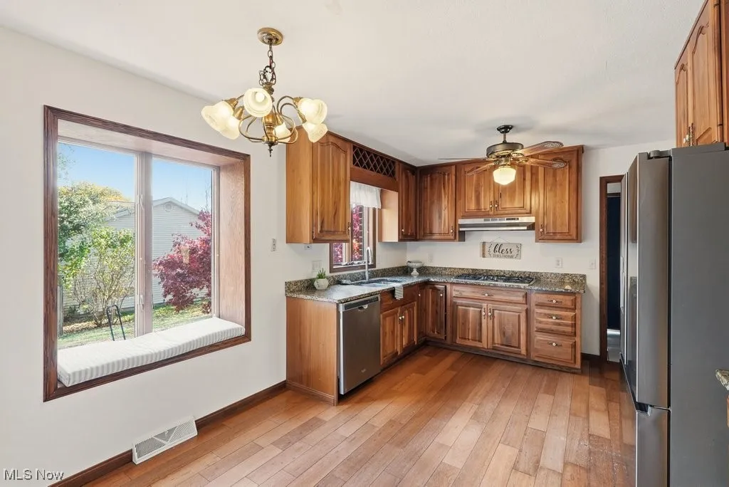 Kitchen featuring stainless steel appliances, brown cabinets, hanging light fixtures, and light wood finished floors
