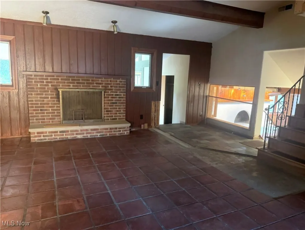 Unfurnished living room with wood walls, a fireplace, stairway, and dark tile patterned floors