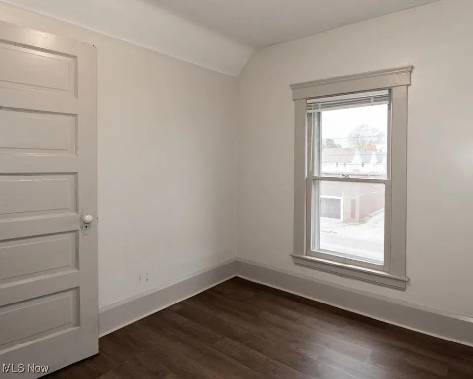 Empty room with dark wood finished floors and vaulted ceiling