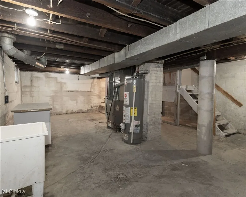 Unfinished below grade area featuring stairway, gas water heater, heating unit, and refrigerator