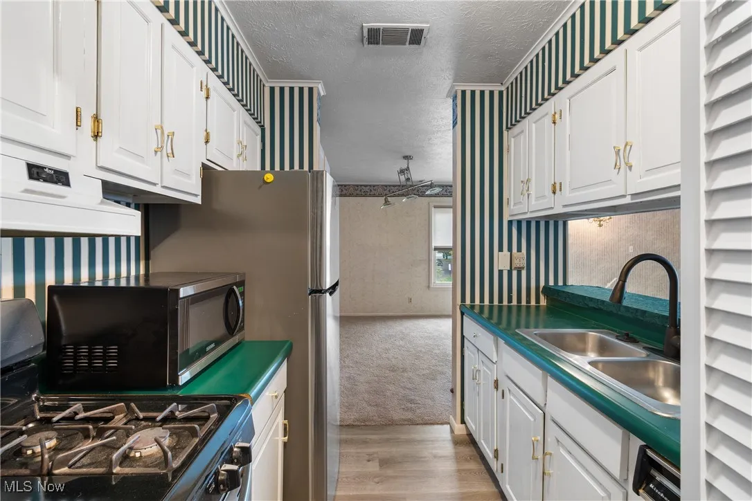 Kitchen featuring wallpapered walls, a textured ceiling, black stove, light wood finished floors, and white cabinets