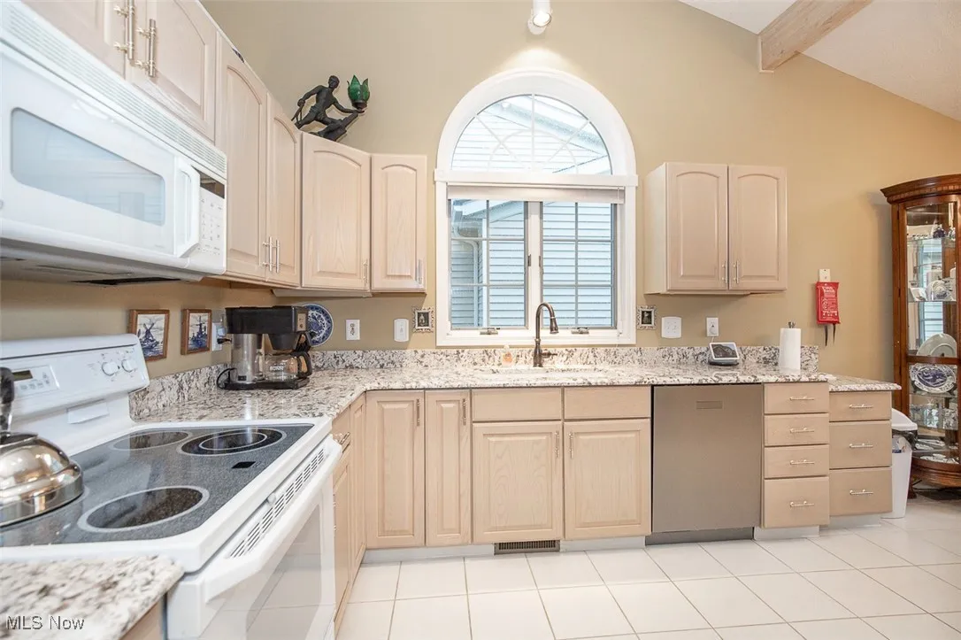 Kitchen featuring white appliances, light brown cabinetry, light stone countertops, and light tile patterned flooring