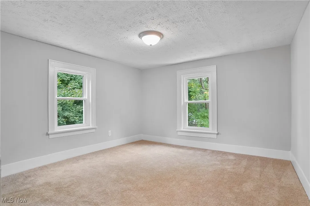 Empty room with light carpet and a textured ceiling