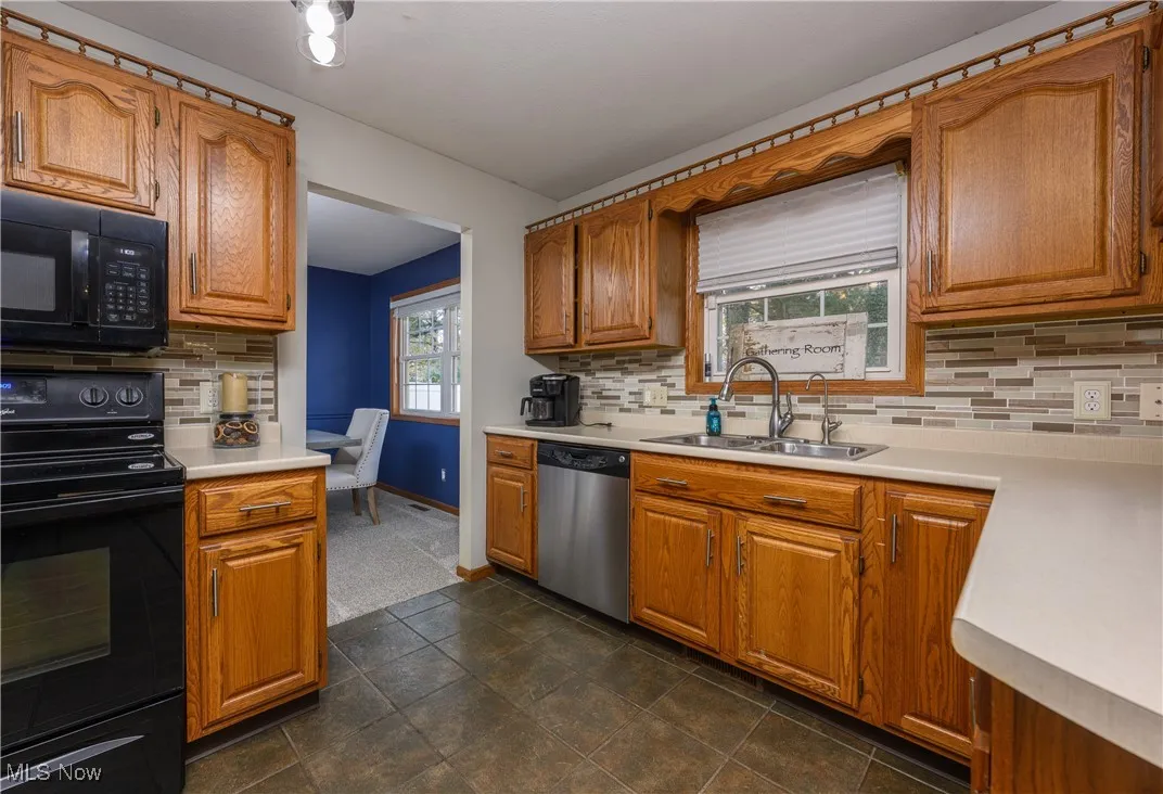 Kitchen featuring black appliances, brown cabinets, decorative backsplash, and light countertops