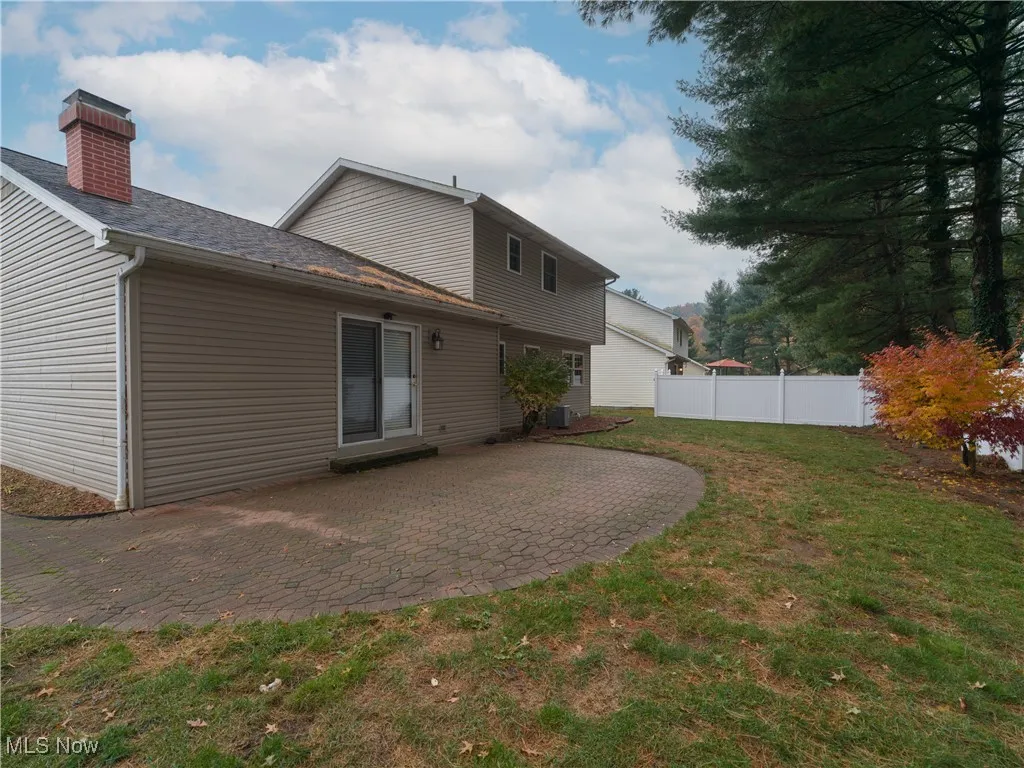 Rear view of house featuring a patio, roof with shingles, and a chimney