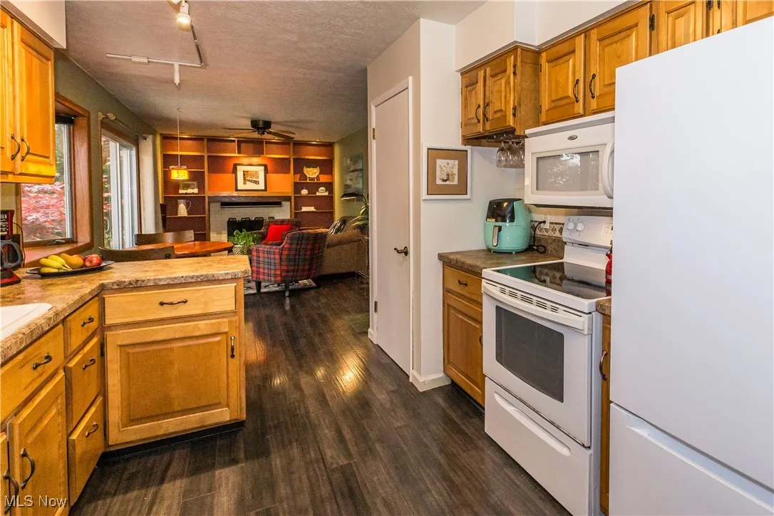 Kitchen featuring white appliances, a fireplace, brown cabinets, a textured ceiling, and laminate finished floors