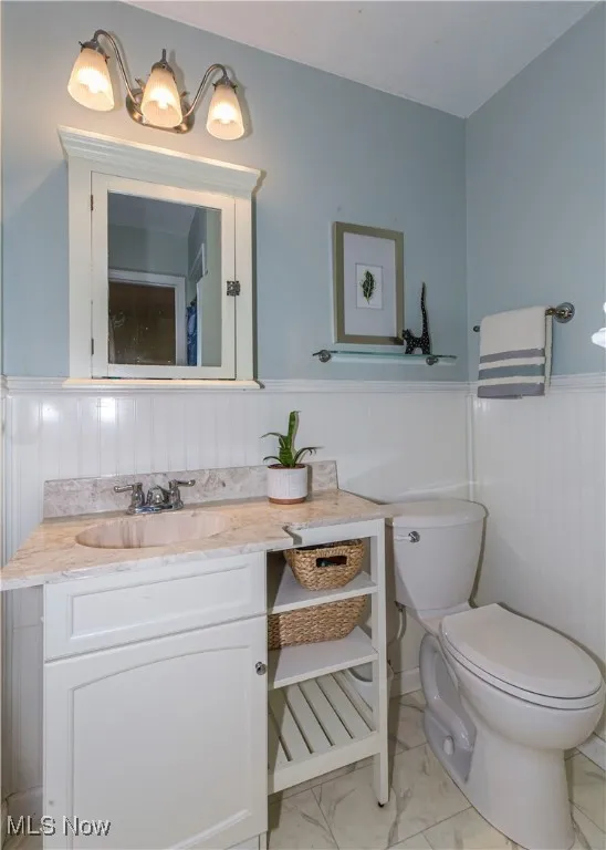 Full bathroom off master bedroom featuring wainscoting, vanity, and light marble finish flooring
