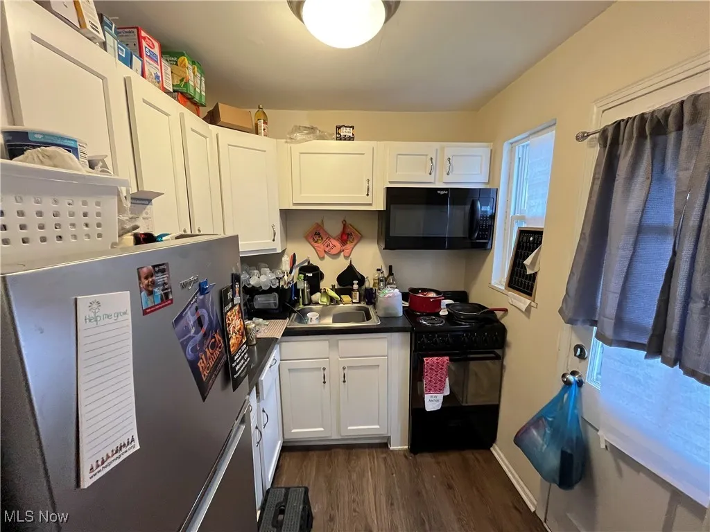 Kitchen with black appliances, dark wood-style floors, white cabinetry, and dark countertops