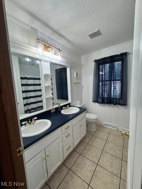 Full bathroom with light tile patterned flooring, double vanity, a shower with curtain, a textured ceiling, and ornamental molding