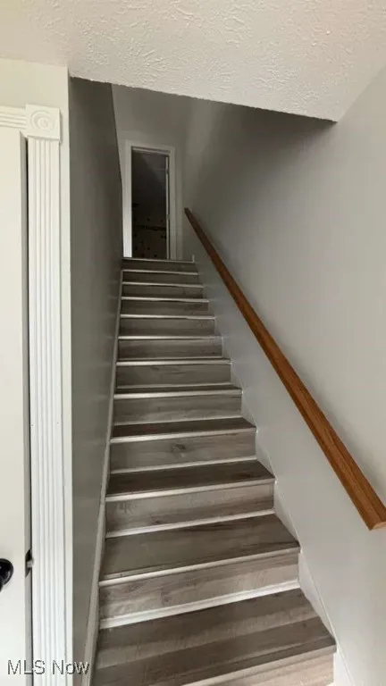 Stairs featuring a textured ceiling and wood finished floors