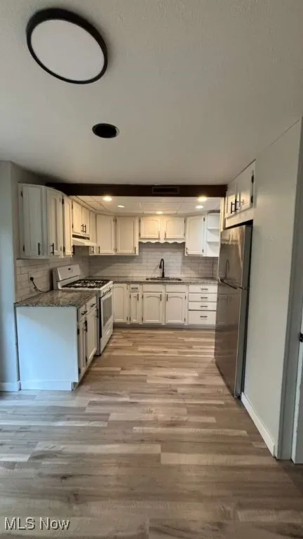 Kitchen with white range with gas cooktop, white cabinetry, decorative backsplash, and freestanding refrigerator