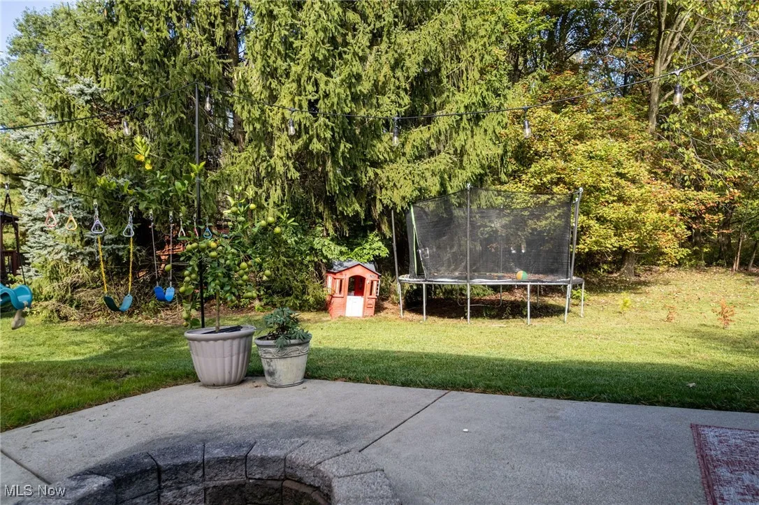 View of patio with a trampoline, a playground, and an outdoor fire pit