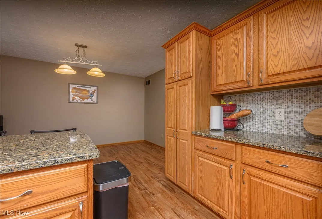 Kitchen featuring dark stone countertops, light wood-style floors, a textured ceiling, pendant lighting, and decorative backsplash