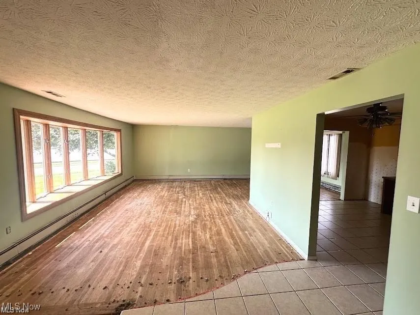 Empty room with a textured ceiling, baseboard heating, light wood finished floors, and a baseboard radiator
