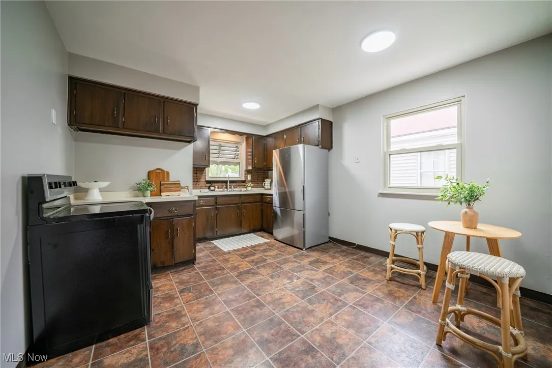 Kitchen featuring light countertops, dark brown cabinets, black electric range oven, and freestanding refrigerator